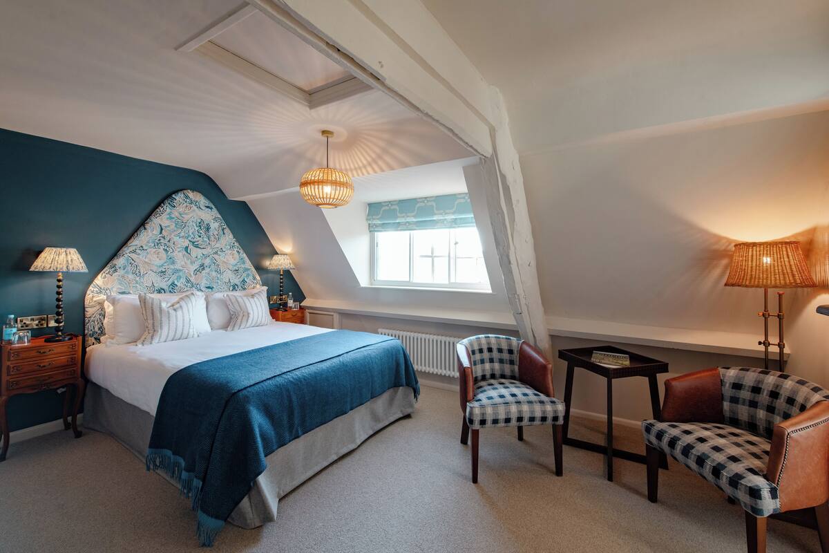 Une chambre avec un grand lit, deux chaises, une petite table et une fenêtre donnant sur un beau paysage.