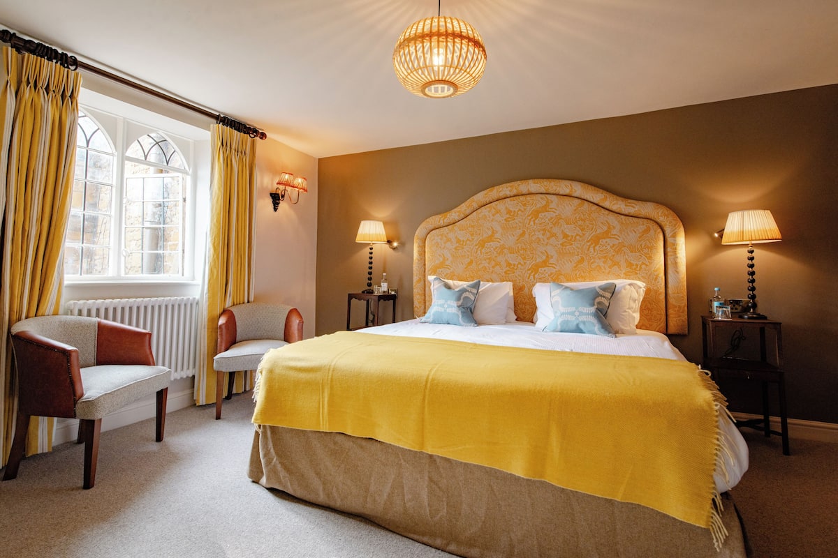 Une chambre d’hôtel avec un grand lit, deux tables de chevet, une chaise et une fenêtre avec des rideaux.