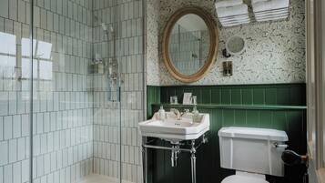 A bathroom with a glass-enclosed shower, a white sink with a green vanity, a toilet, and a mirror above the sink.