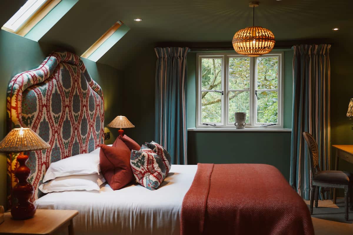 Une chambre avec un grand lit, une fenêtre avec des rideaux, une table avec une lampe et une chaise.