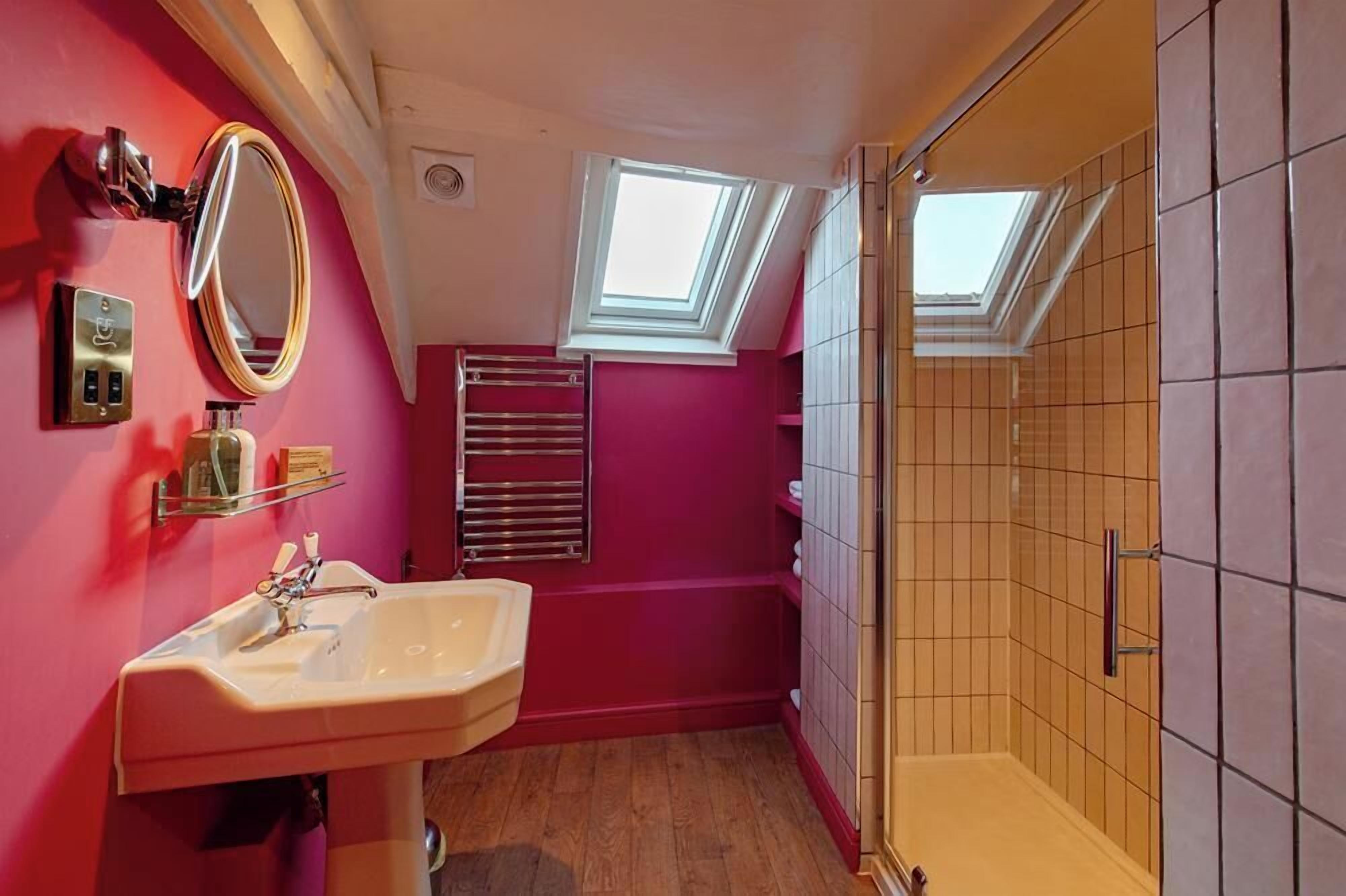 A bathroom with a pink wall, a white sink, a mirror, a towel rack, and a skylight.