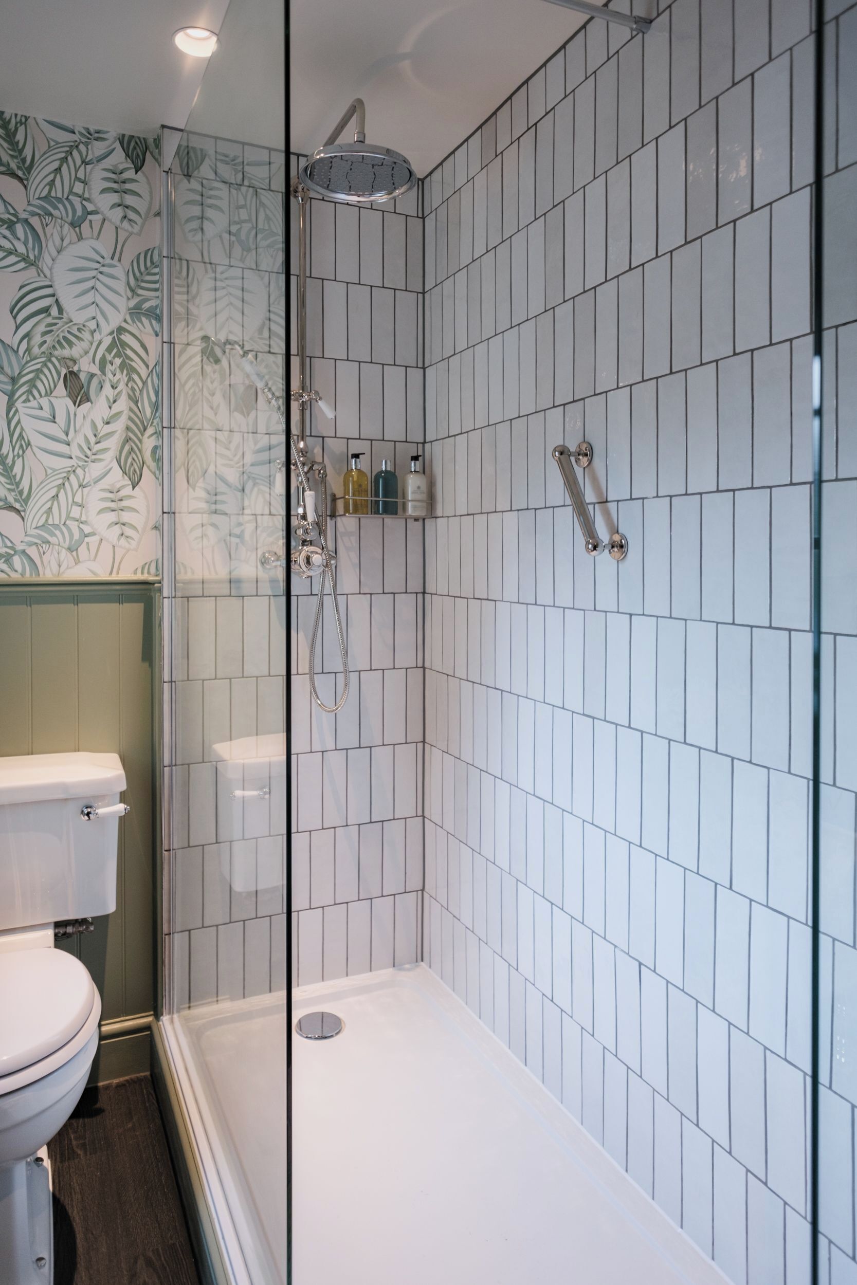 A modern bathroom with a glass-enclosed shower, white tiled walls, and a toilet.