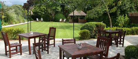 Eine Terrasse im Freien mit Holztischen und -stühlen, einer Laube und einem gepflegten Rasen.