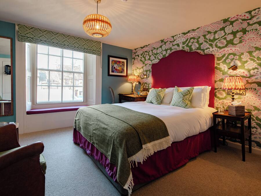 A bedroom with a large bed, a window with a view, a bedside table with lamps, and a mirror.