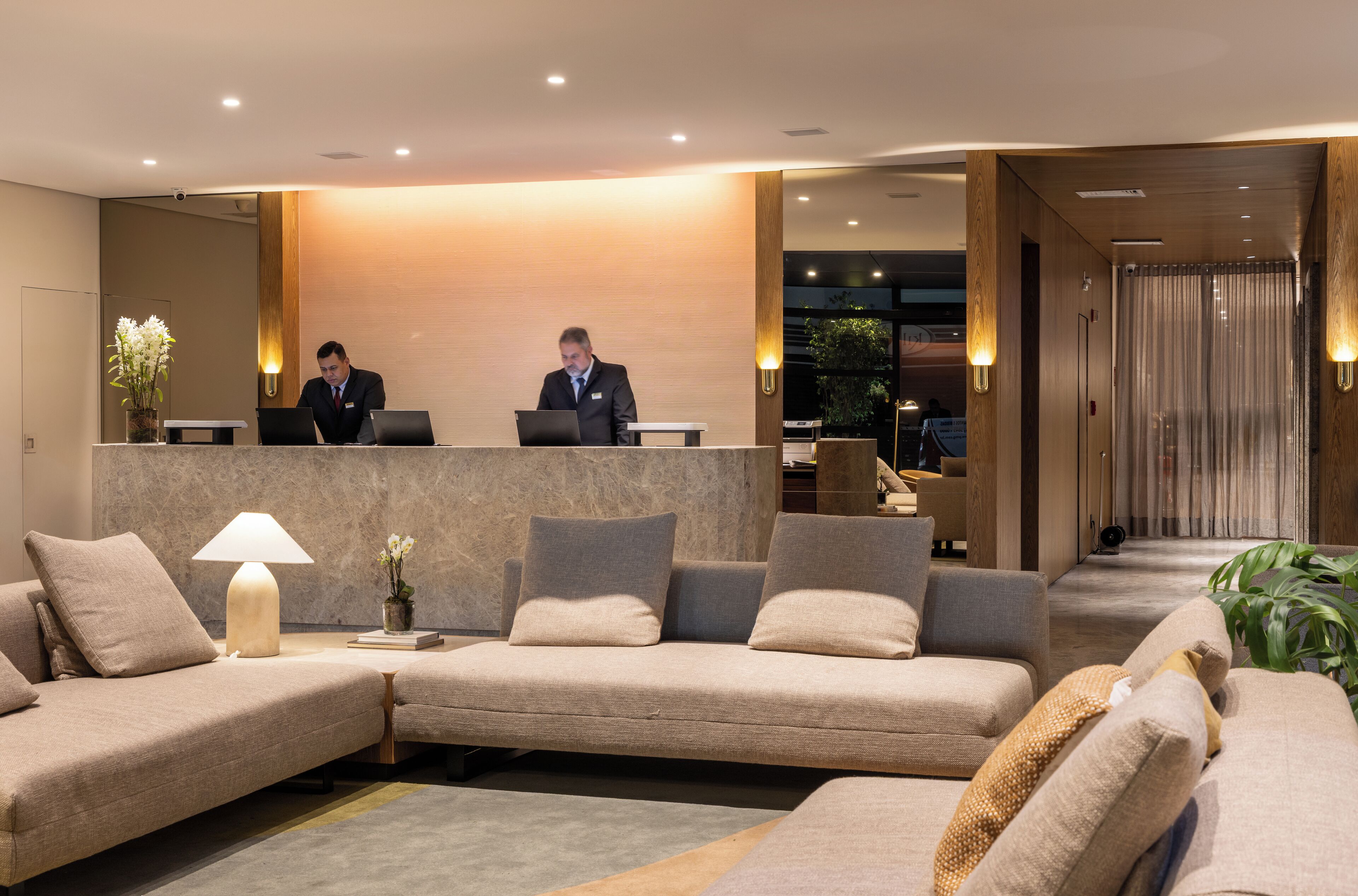 A modern hotel lobby with a reception desk, sofas, a lamp, and a mirror.