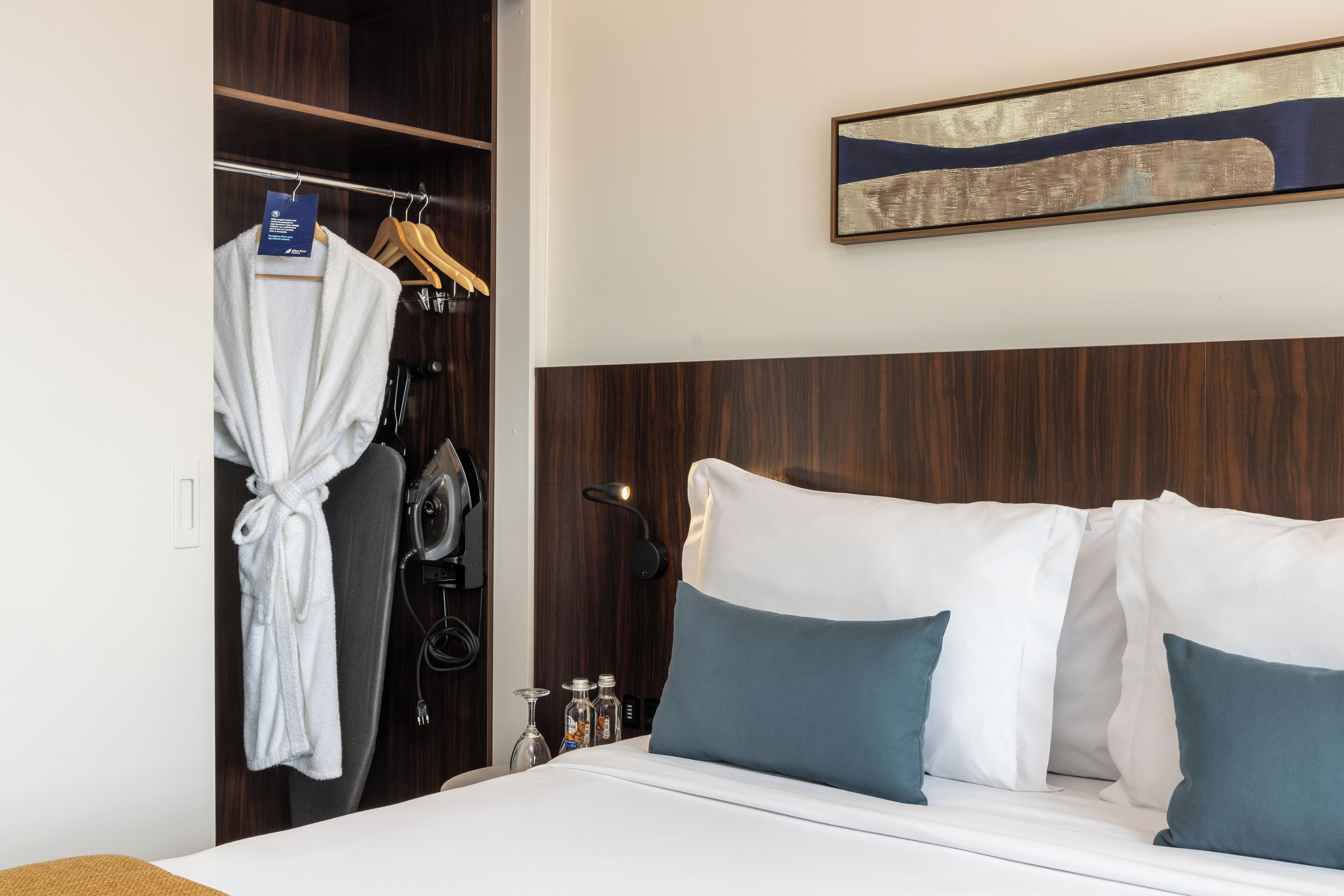A hotel room with a bed, a robe hanging on a rack, and a wall-mounted artwork.