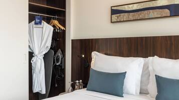 A hotel room with a bed, a robe hanging on a rack, and a wall-mounted artwork.