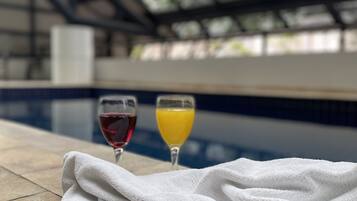 A poolside setting with a glass of red wine and orange juice, a towel, and sunglasses on a magazine.