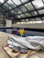 A poolside setting with a glass of red wine and orange juice, a towel, and sunglasses on a magazine.