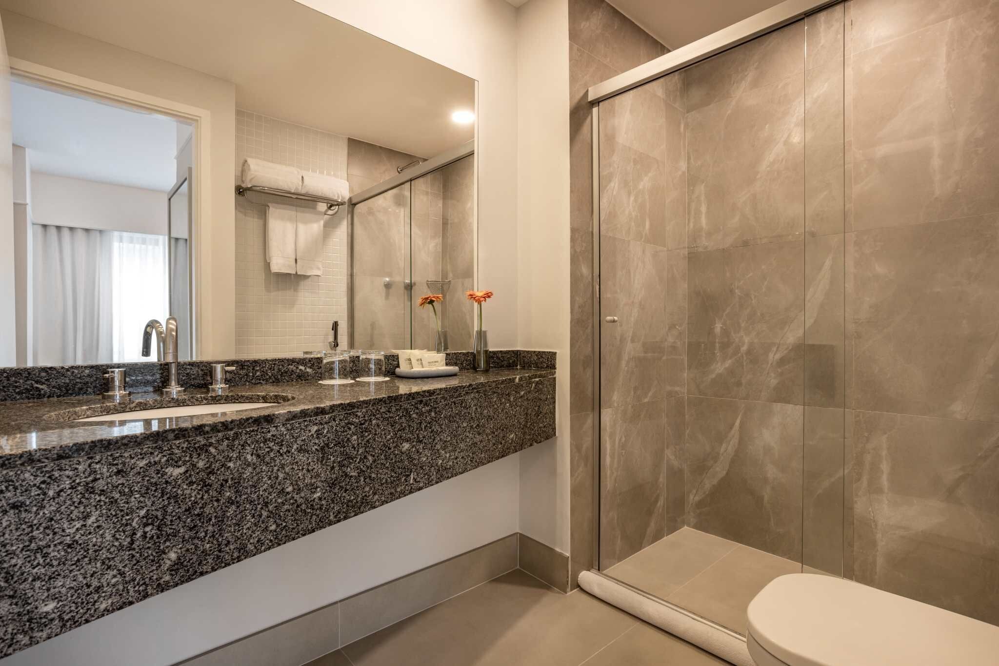 Une salle de bain moderne avec un comptoir en granit, une cabine de douche en verre et des toilettes.