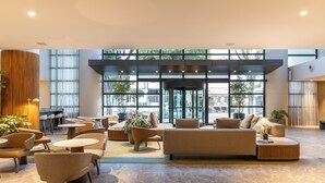 Un hall espacioso con diseño moderno, que incluye un amplio espacio de descanso con sofás y sillones, una mesa de centro y una planta en maceta.
