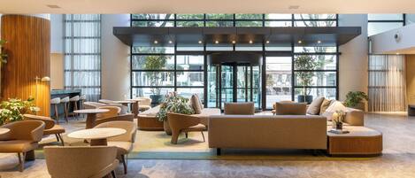 A spacious lobby with a modern design, featuring a large seating area with sofas and chairs, a coffee table, and a potted plant.