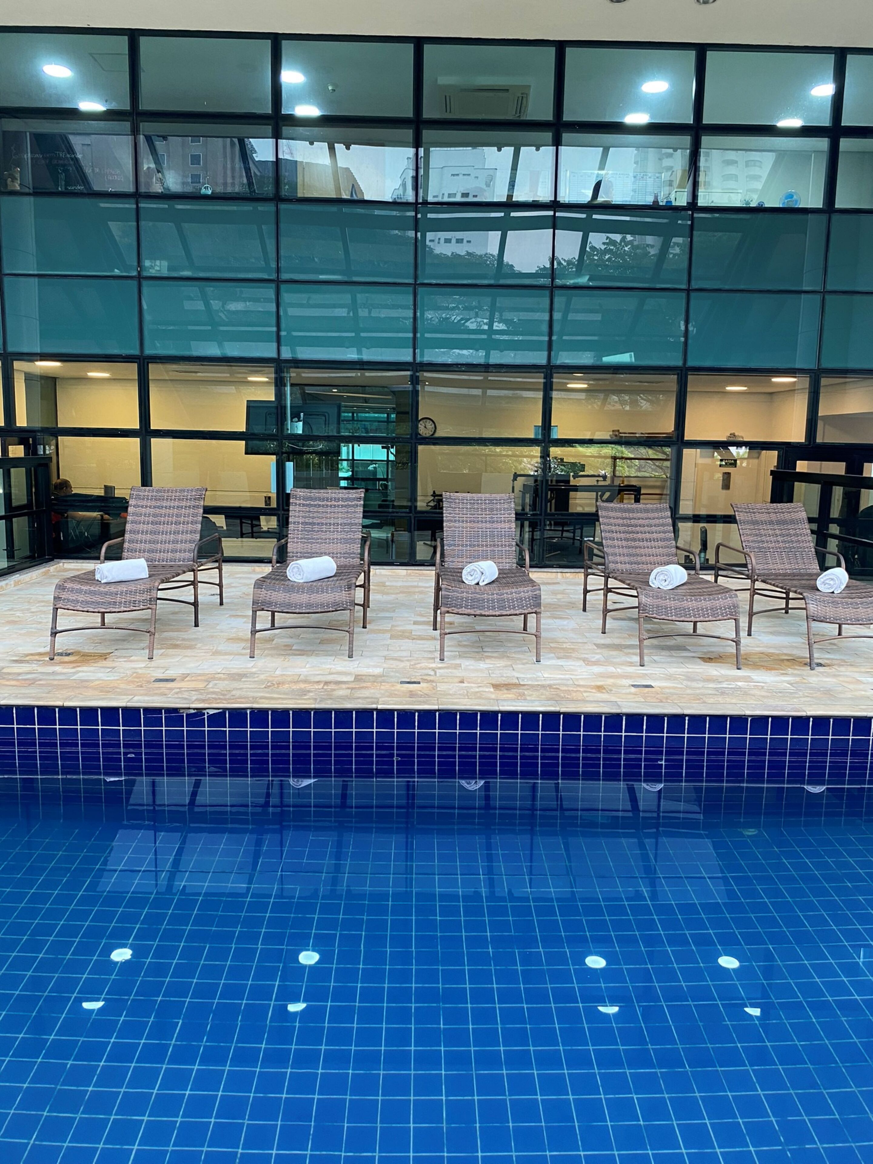 Un espace piscine avec des chaises longues et une vue sur l’intérieur grâce à de grandes fenêtres.
