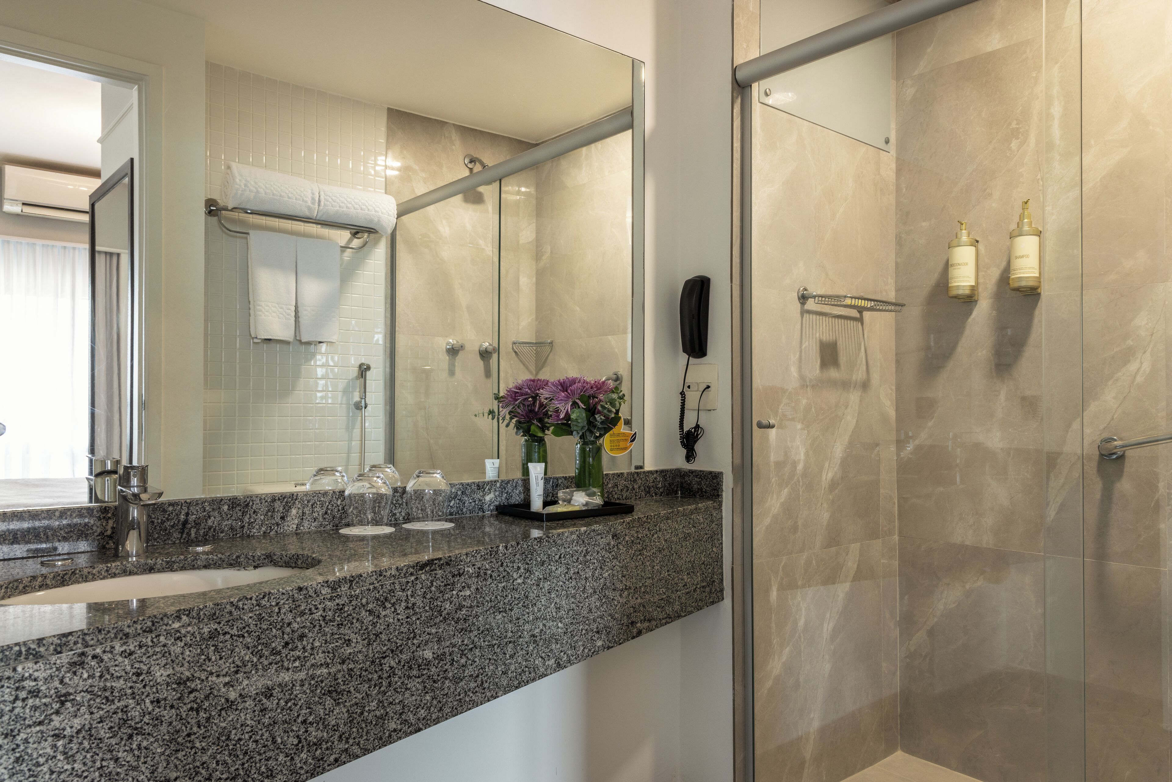 Un baño moderno con encimera de granito, cabina de ducha de vidrio y un espejo grande.