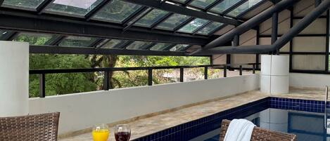 A covered outdoor seating area with a pool, featuring a table with drinks and a menu, and wicker chairs.
