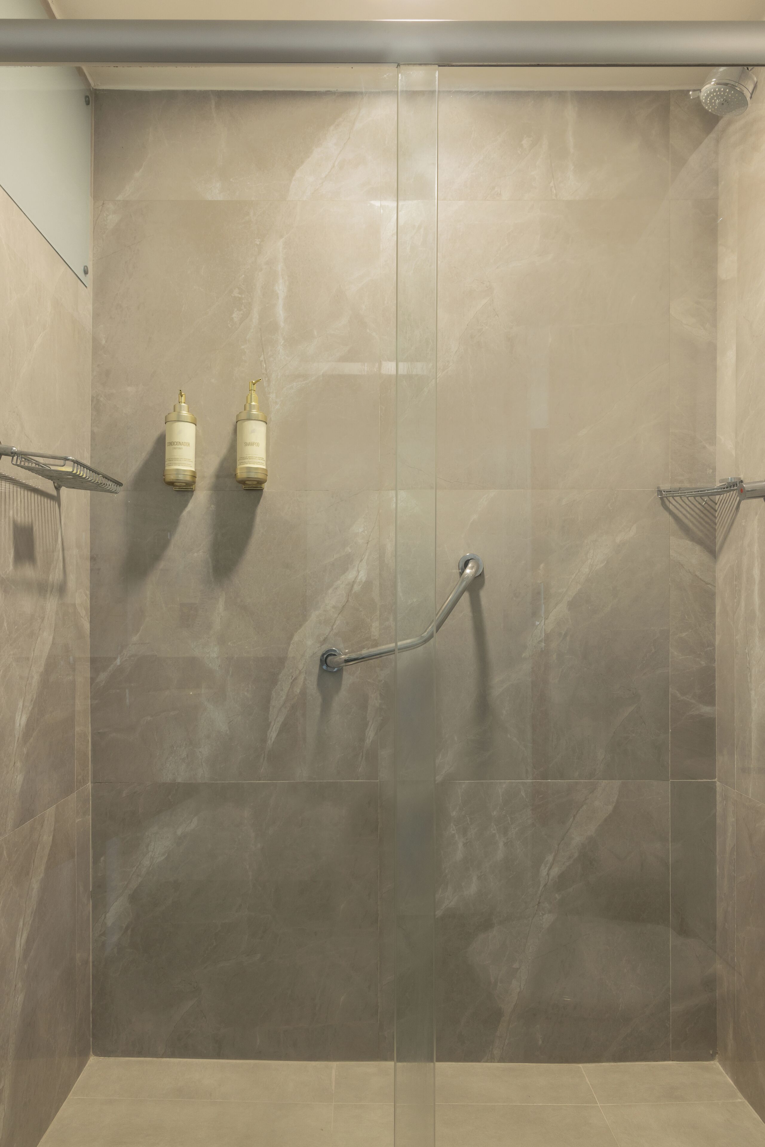 A walk-in shower with a glass door, a handheld showerhead, and two wall-mounted soap dispensers.