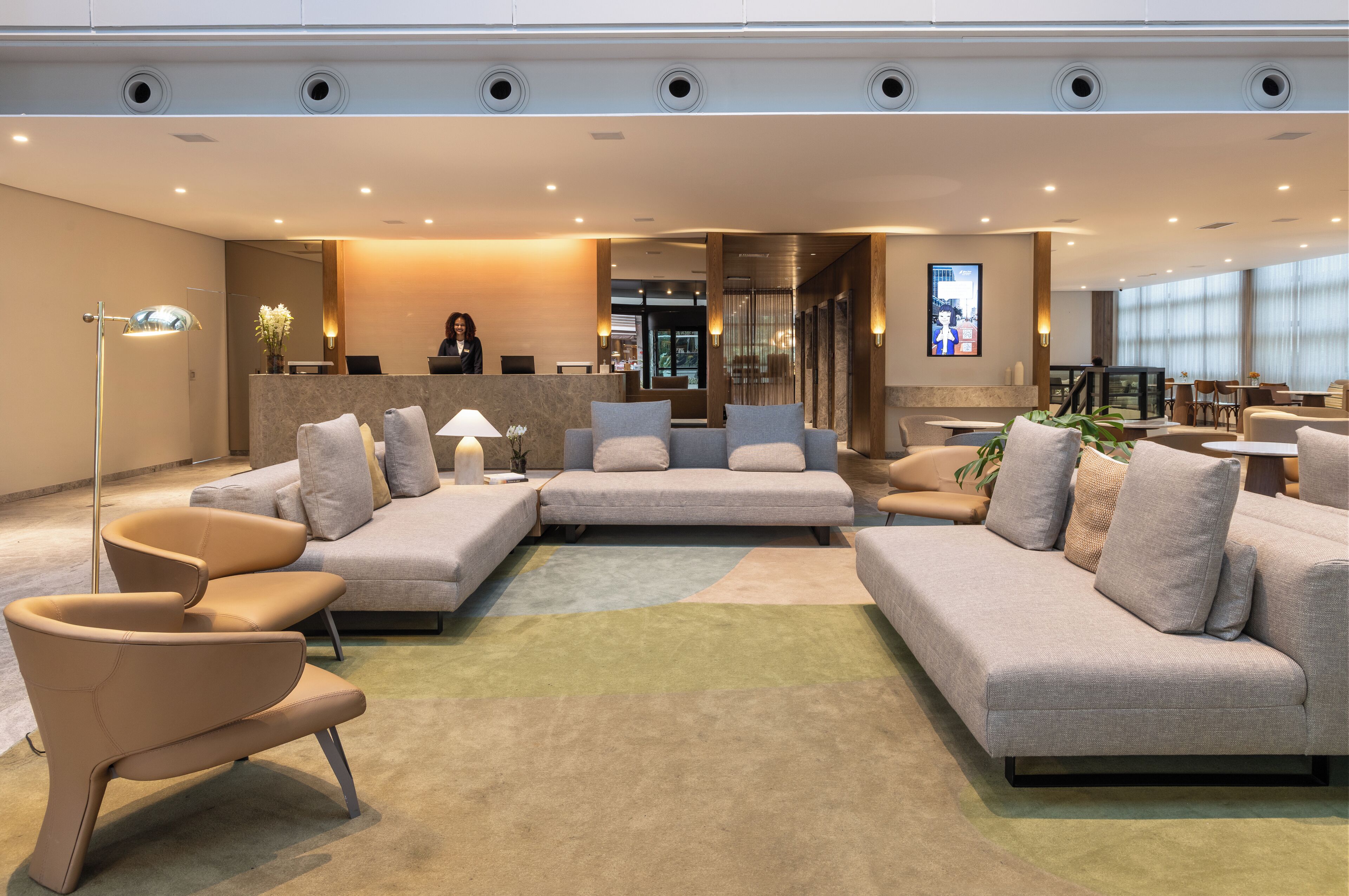 A modern hotel lobby with a reception desk, seating area, and a dining space.