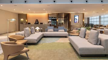 A modern hotel lobby with a reception desk, seating area, and a dining space.