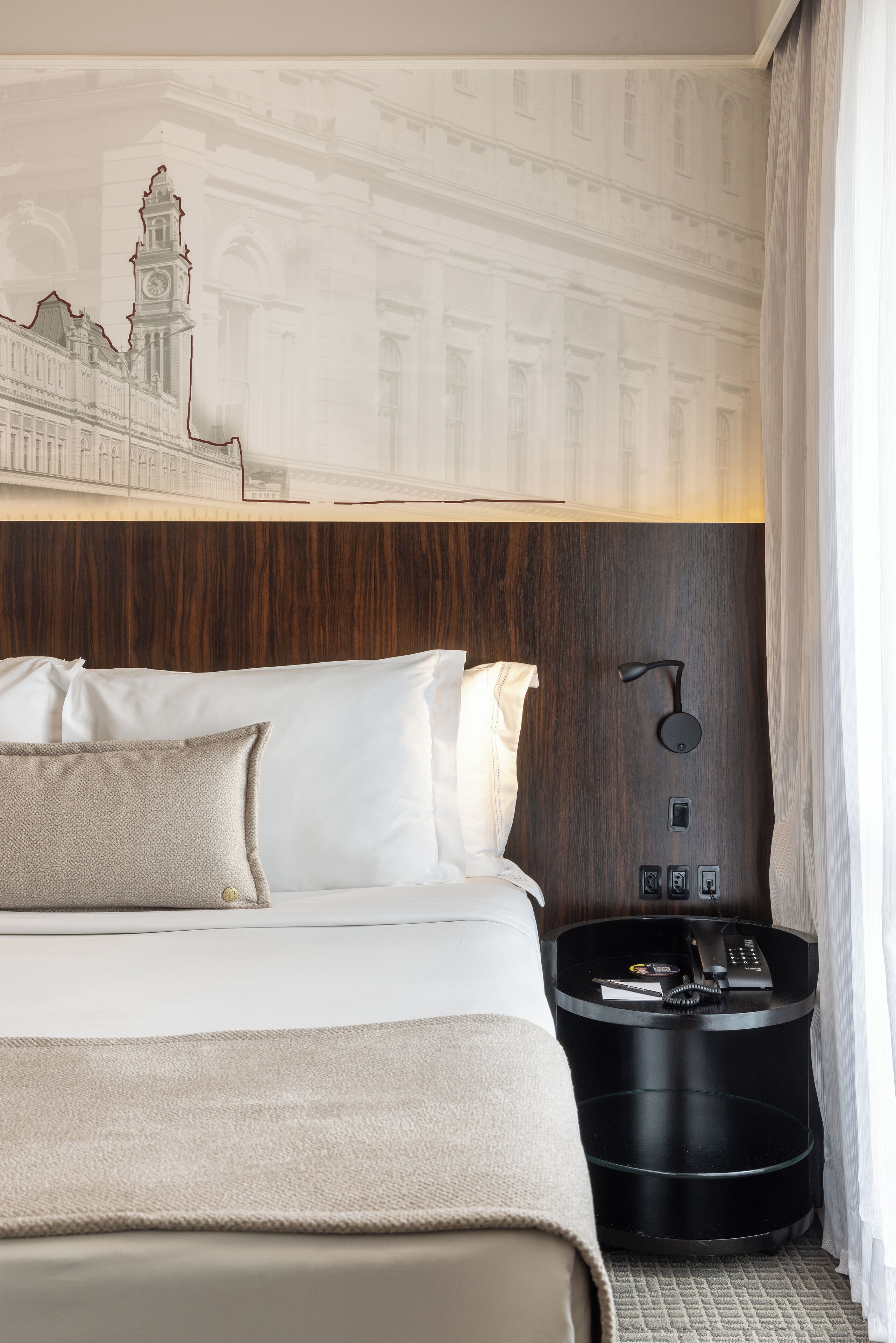 Et hotelværelse med en stor seng, et træhovedgærde, et natbord med en lampe og et vægmaleri.