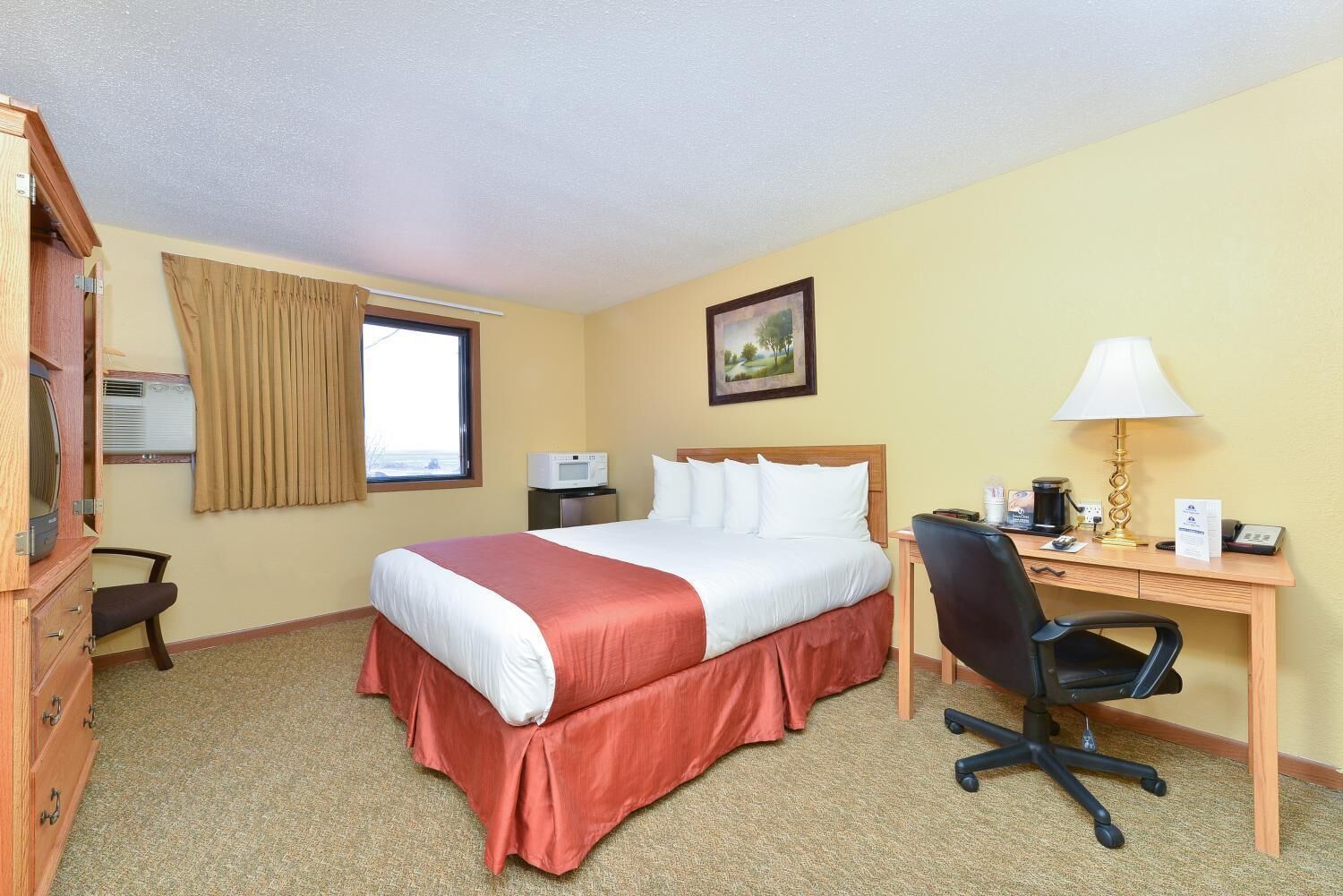 Habitación de hotel con cama, escritorio, silla y ventana con cortinas.