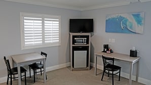 A hotel room with a dining table, two chairs, a microwave, a refrigerator, a coffee maker, and a painting of a wave on the wall. - Surf City Inn - Near Seal Beach Pier (Seal Beach)