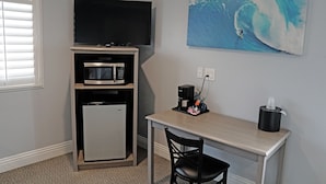 A compact kitchenette with a microwave, refrigerator, and coffee maker. A flat-screen TV is mounted above the microwave. There's a painting of a surfer on a wave on the wall. - Surf City Inn - Near Seal Beach Pier (Seal Beach)
