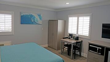A hotel room with a bed, a desk with a chair, a wardrobe, a television, and a painting on the wall.