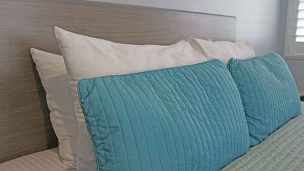 A bed with a wooden headboard, white and teal pillows, and a quilted blanket. - Surf City Inn - Near Seal Beach Pier (Seal Beach)