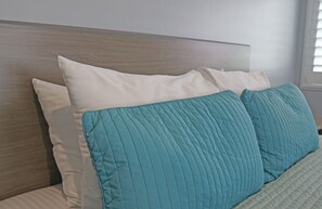 A bed with a wooden headboard, white and teal pillows, and a quilted blanket. - Surf City Inn - Near Seal Beach Pier (Seal Beach)