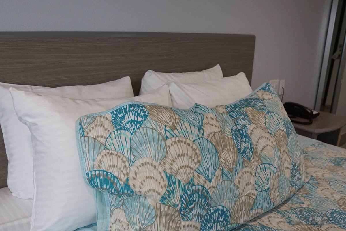 A bed with white pillows and a patterned blanket, a wooden headboard, and a bedside table with a telephone.