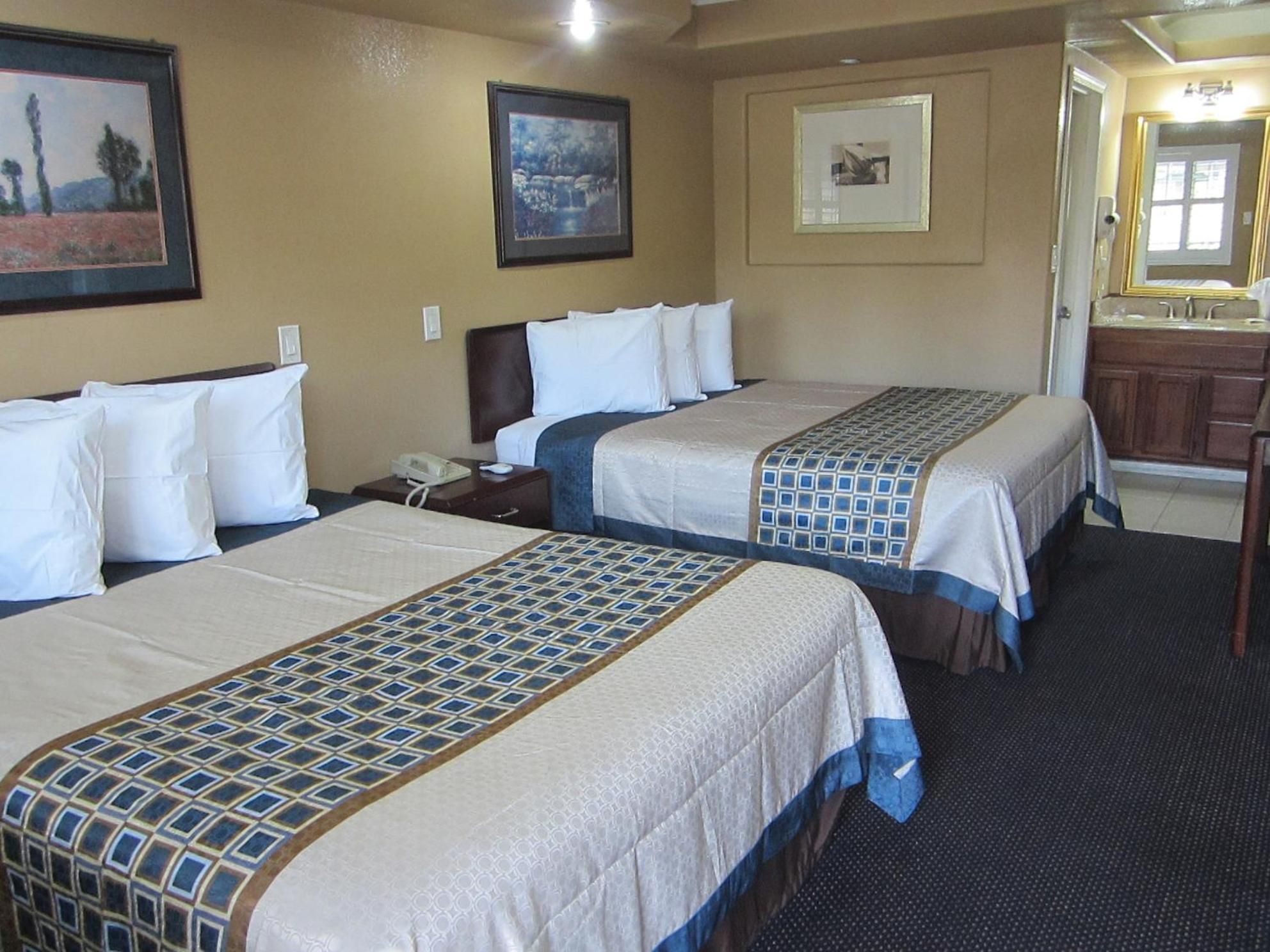A hotel room with two beds, a desk, a chair, and a bathroom visible through an open door.