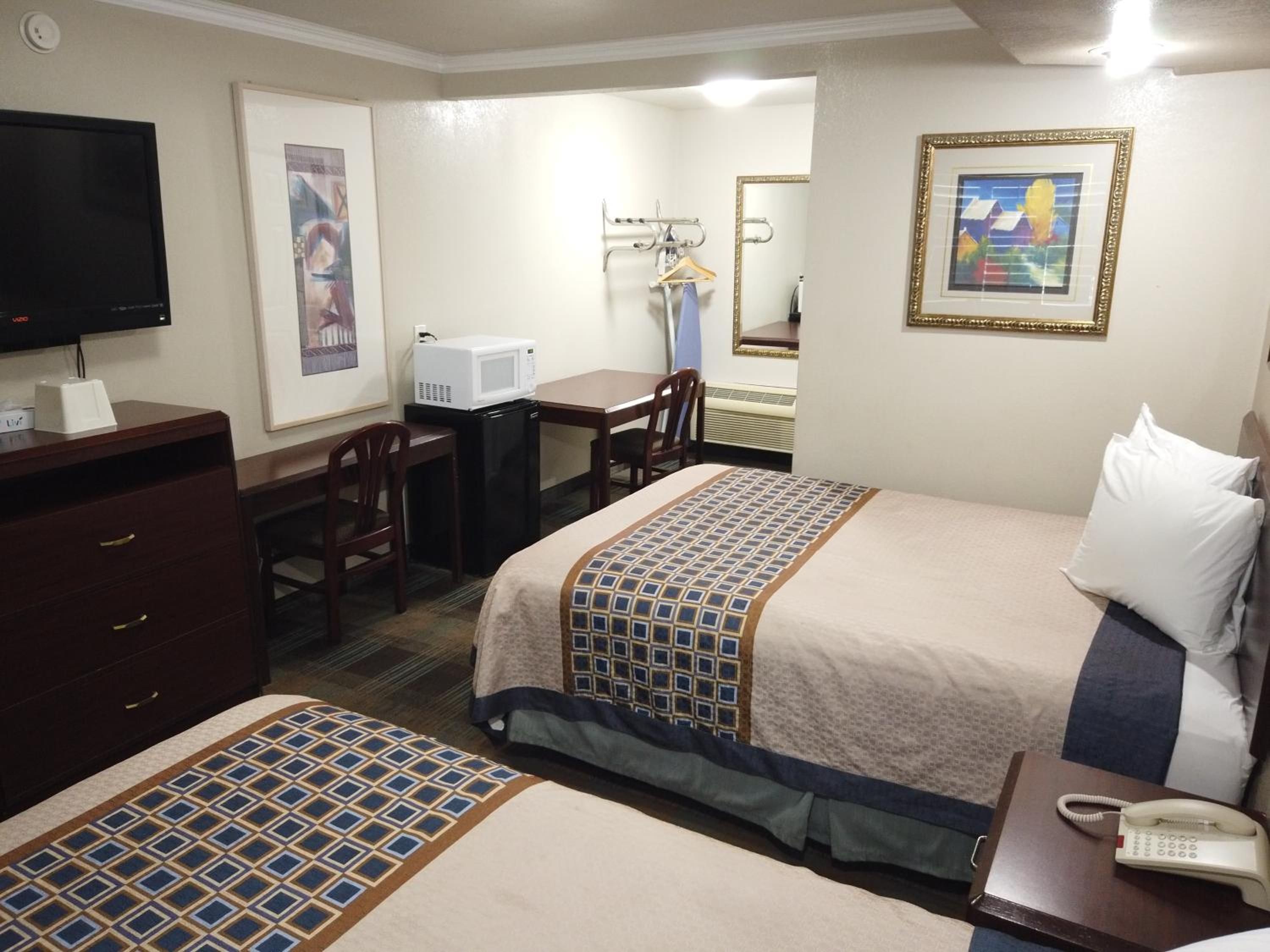 A hotel room with two beds, a desk, a television, a microwave, and a telephone.