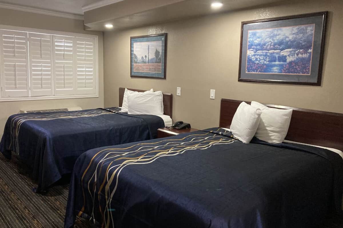 A hotel room with two beds, a window with blinds, and two framed pictures on the wall.