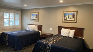 A hotel room with two beds, a window with blinds, a nightstand, and two framed pictures on the wall.