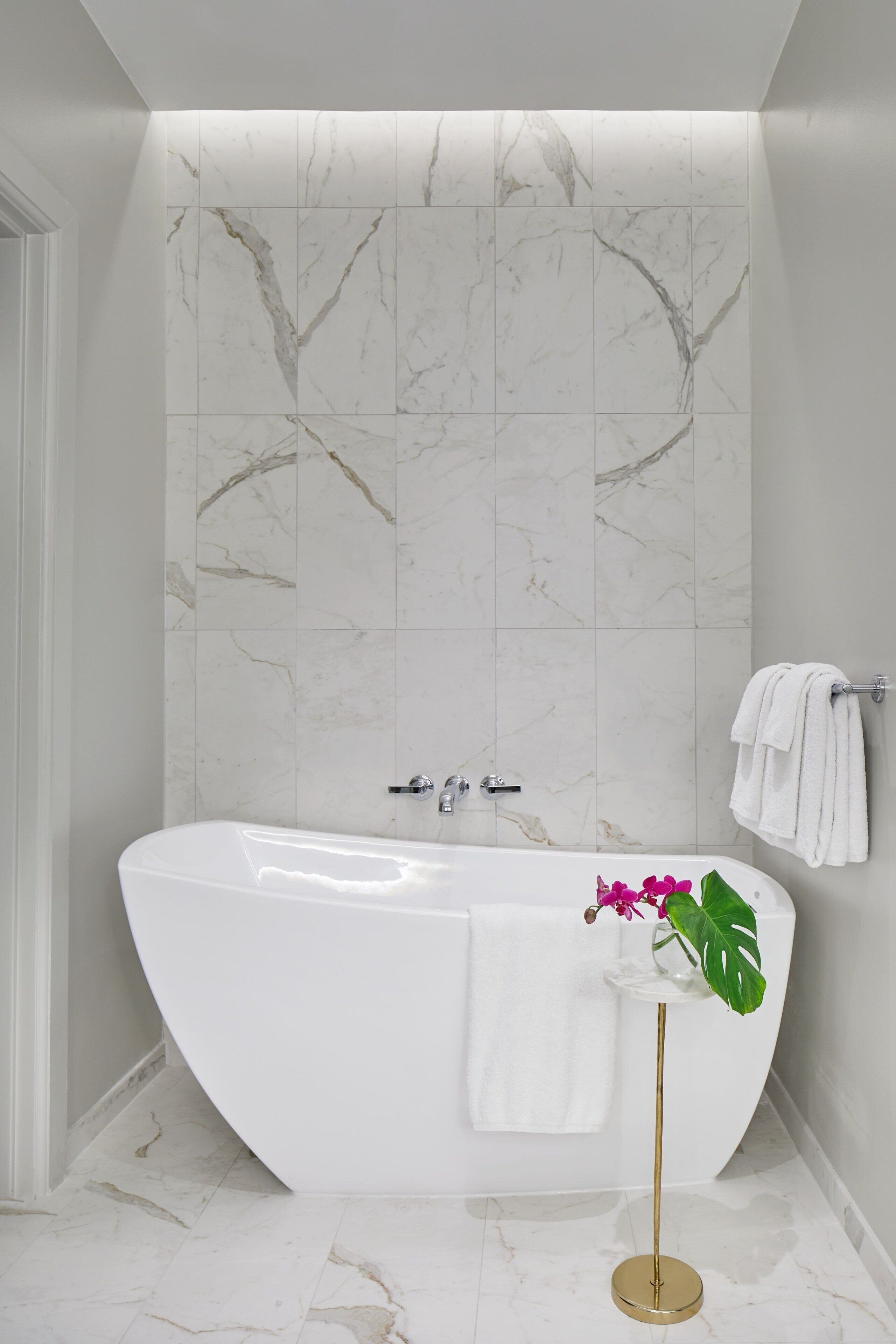Een moderne badkamer met een vrijstaand bad, marmeren tegels en een potplant.