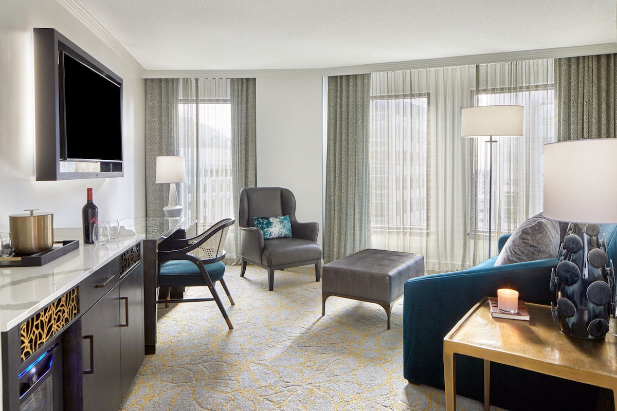 Une chambre d’hôtel moderne équipée d’une télévision à écran plat, d’un canapé, d’un fauteuil, d’une petite table avec une bougie et d’un vase décoratif.