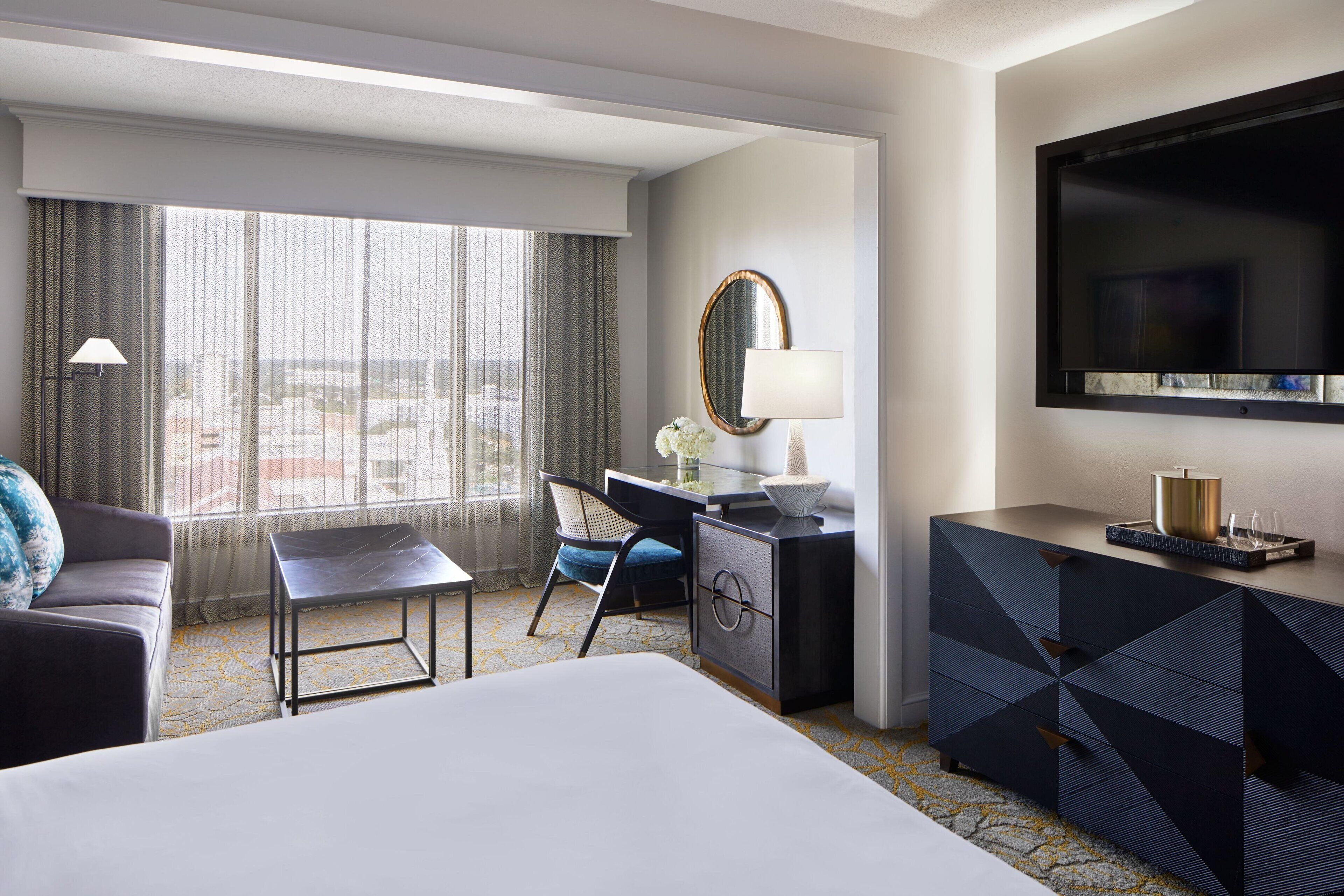 Une chambre d’hôtel équipée d’un lit, d’un bureau, d’une chaise, d’une commode, d’une télévision et d’une fenêtre avec des rideaux.
