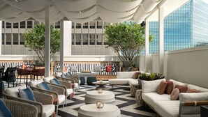 A modern outdoor seating area with wicker furniture, a white sofa, and round tables. - Grand Bohemian Orlando, Autograph Collection (Orlando)