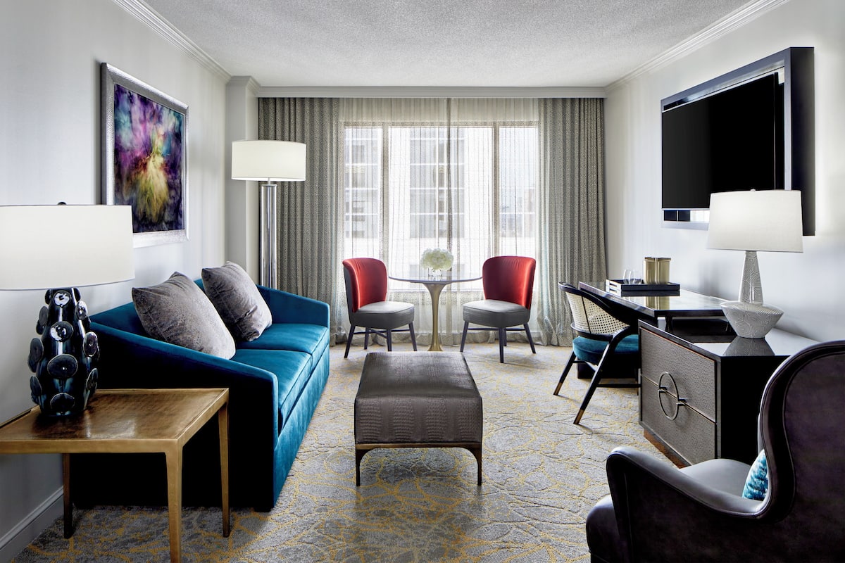 Une chambre d’hôtel avec un canapé bleu, deux fauteuils rouges, une petite table, un téléviseur et un bureau avec une lampe.