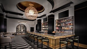 A bar area with a long counter, multiple stools, and a chandelier. - Hotel Beauden, Autograph Collection (Orlando)