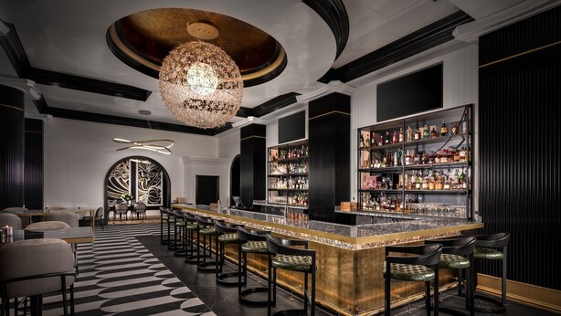 A bar area with a long counter, multiple stools, and a chandelier. - Grand Bohemian Orlando, Autograph Collection (Orlando)