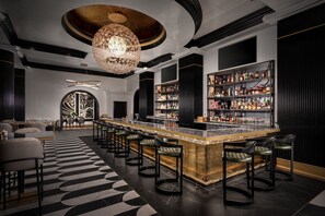A bar area with a long counter, multiple stools, and a chandelier. - Hotel Beauden, Autograph Collection (Orlando)