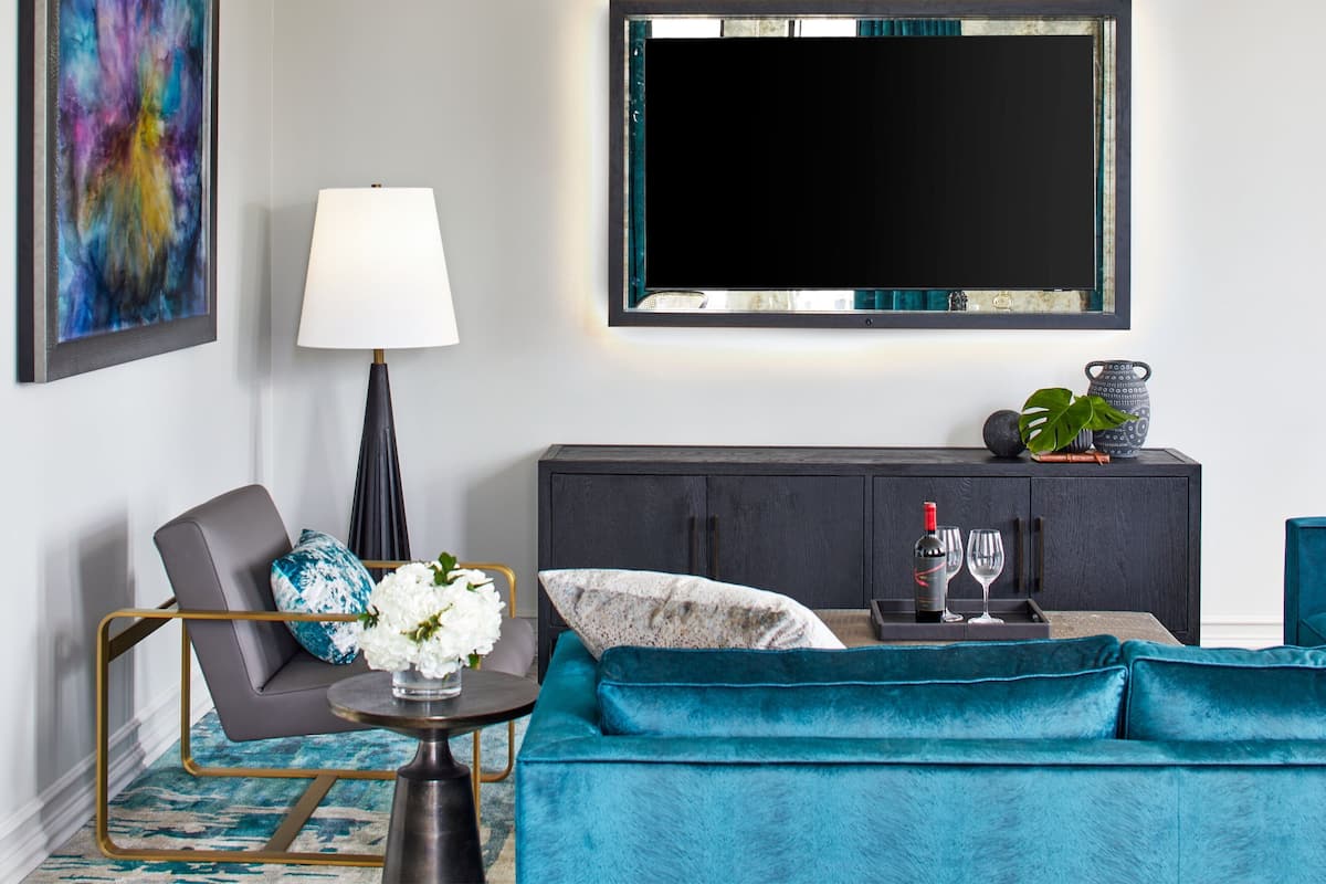 Un salon moderne avec un canapé de couleur turquoise, un fauteuil gris, une table basse, un téléviseur fixé au mur et un meuble contenant des objets décoratifs.