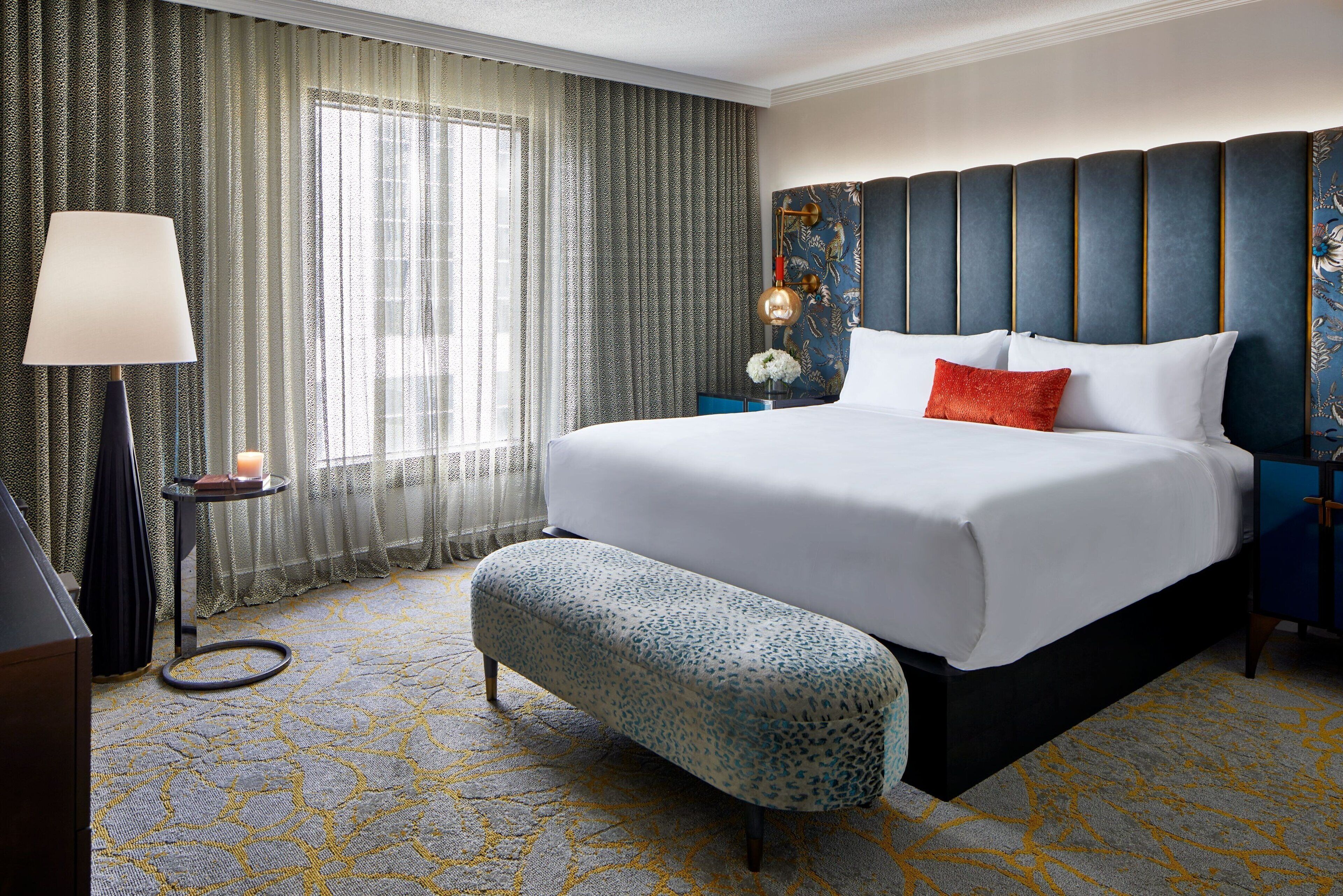 A hotel room with a large bed, a bench, a lamp, and a nightstand with a candle.