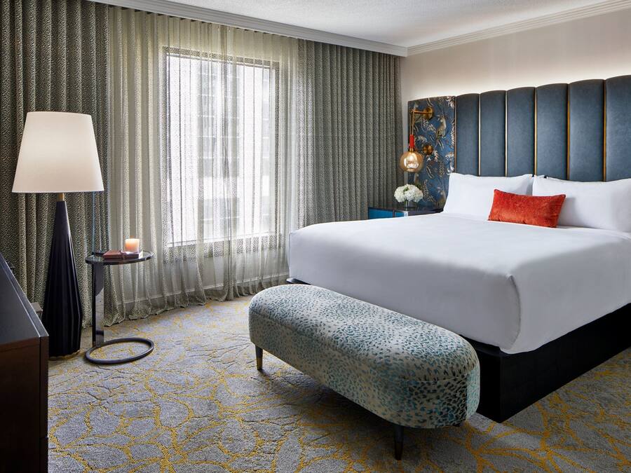 A hotel room with a large bed, a bench, a lamp, and a nightstand with a candle.