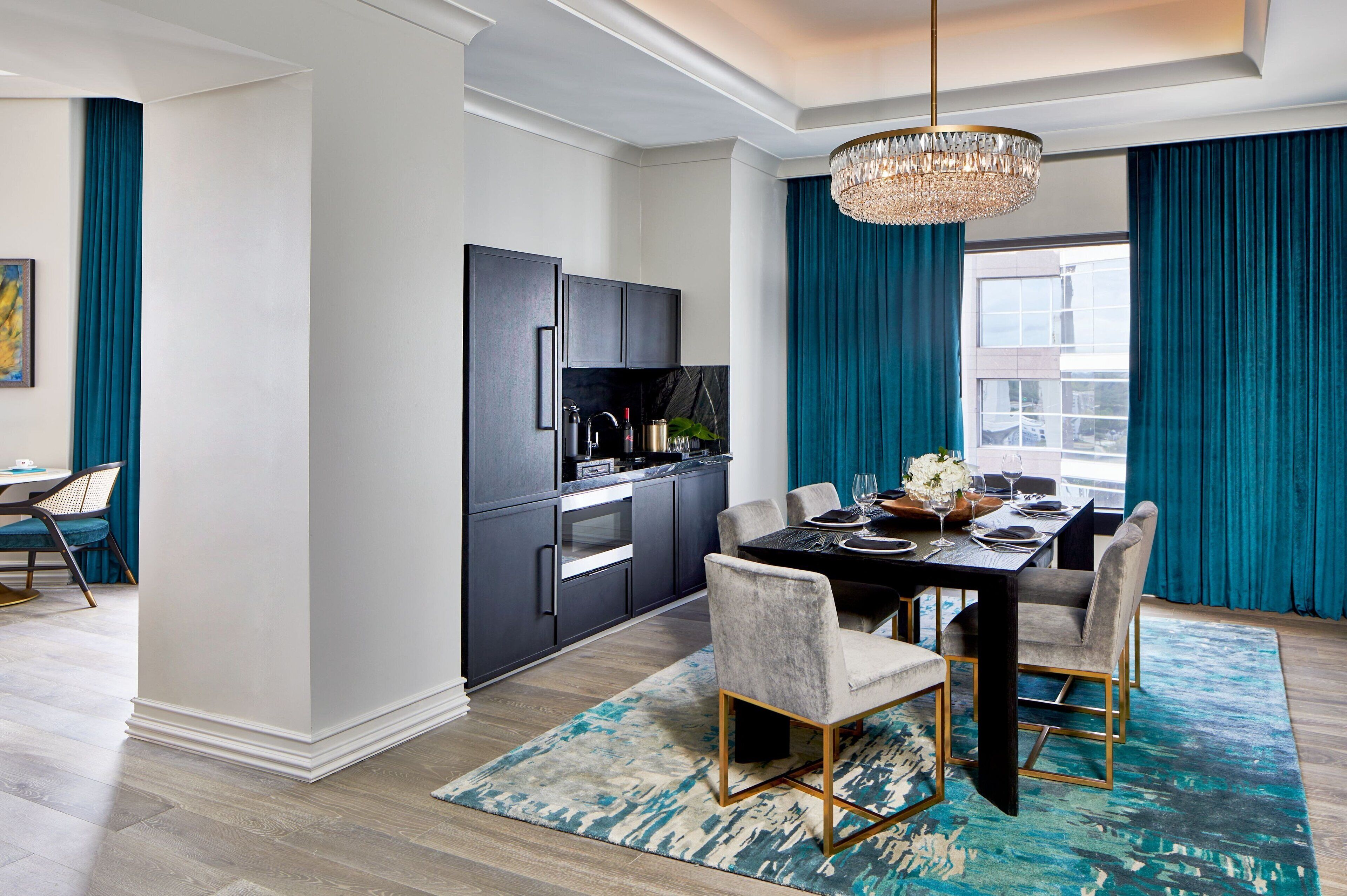 Une cuisine moderne avec des meubles de couleur sombre, un coin repas doté d’une table noire et des rideaux turquoise.