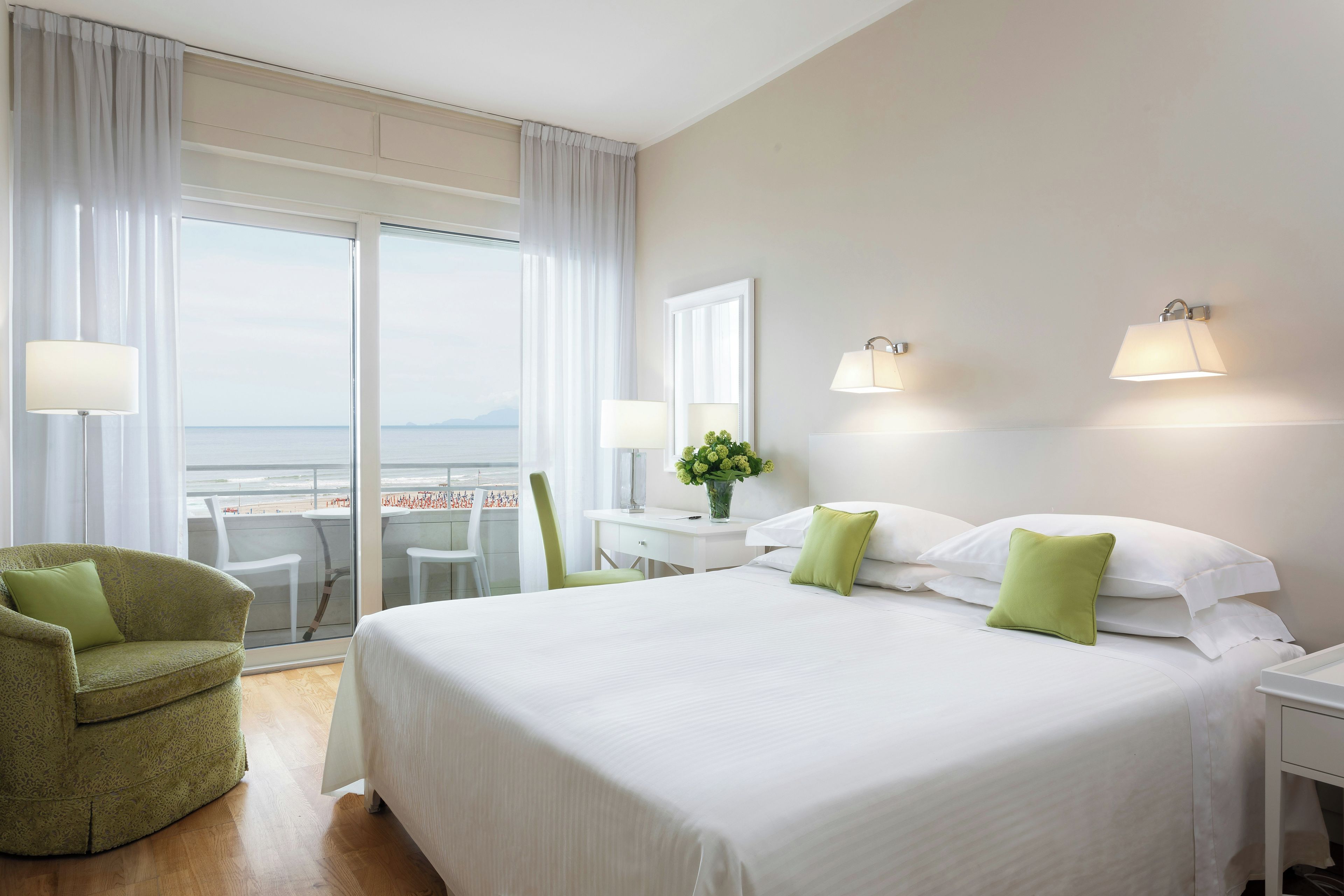 A hotel room with a large bed, a desk, a chair, and a view of the sea.