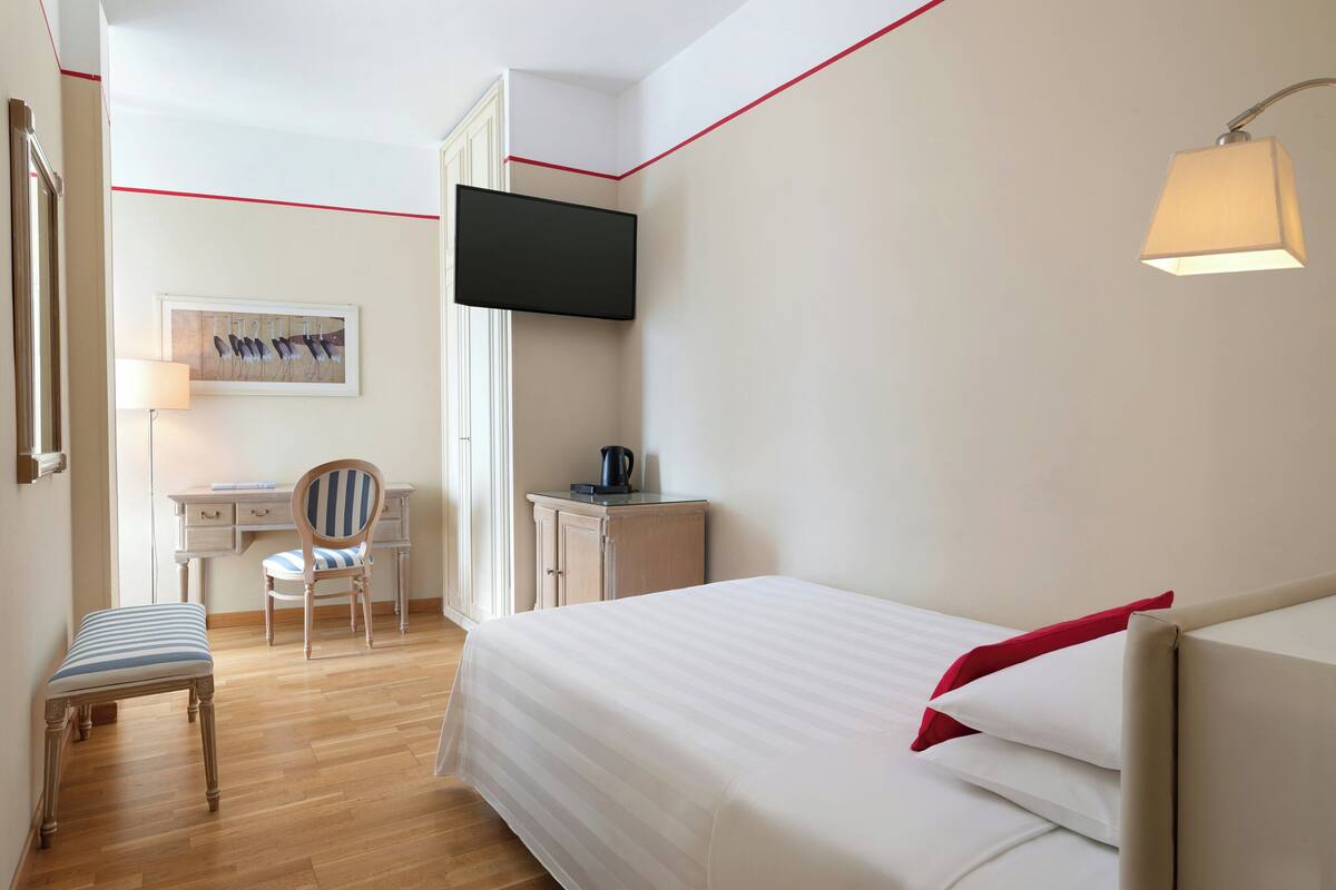 A hotel room with a bed, a desk with a chair, a television, and a lamp.