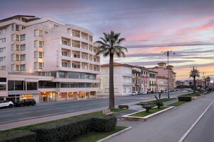 Un hotel de varios pisos con un llamativo letrero 'ASTOR', una calle bien cuidada y un cielo al atardecer.