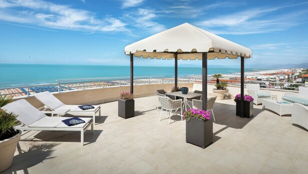 A rooftop terrace with a gazebo, lounge chairs, a table, and potted plants. - Sina Astor (Viareggio)